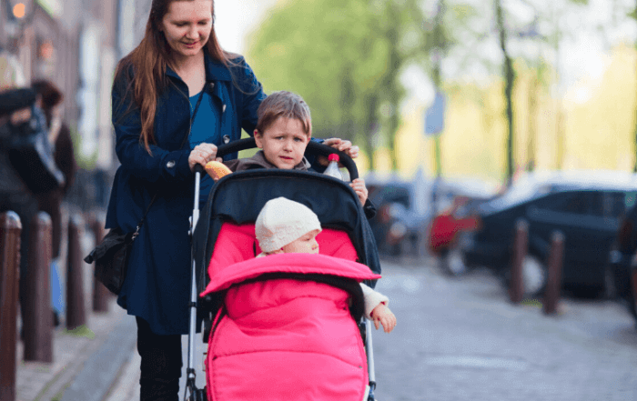 woman with children in a sit and stand stroller on a city street